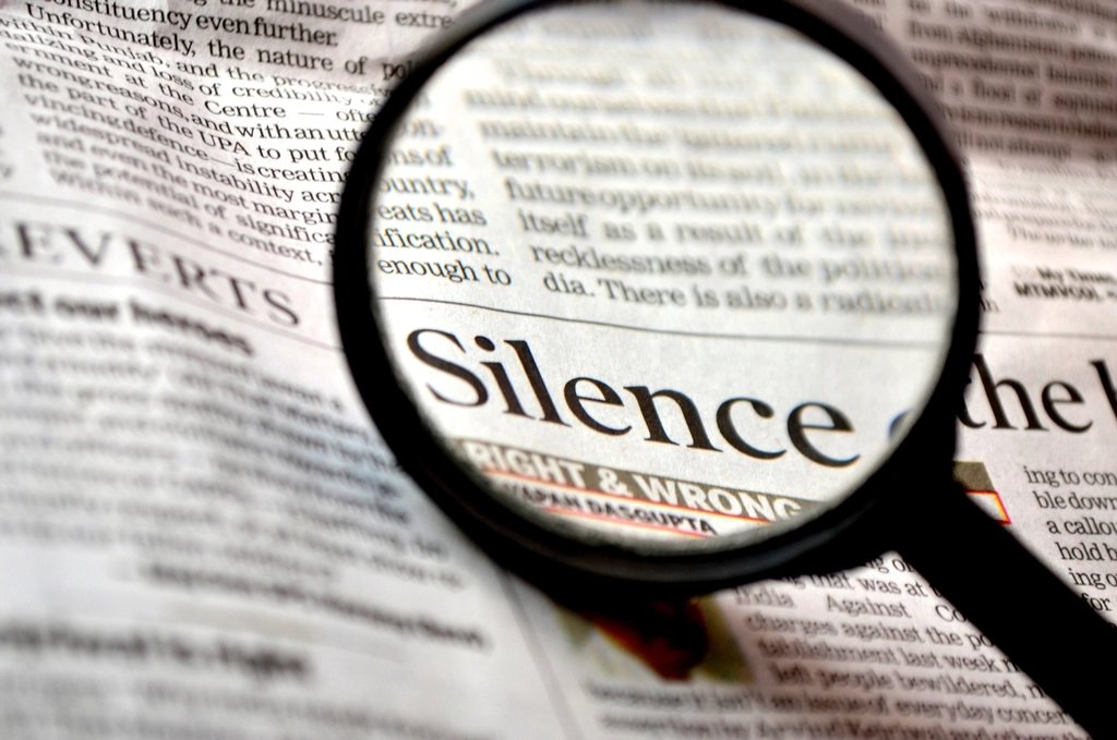 Лупа над газетным заголовком «Silence» на странице с мелким текстом