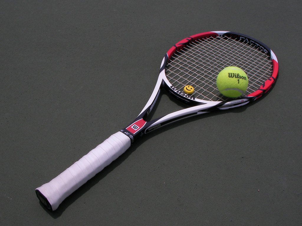 Теннисная ракетка Wilson с белой обмоткой и жёлтый мяч на тёмном корте